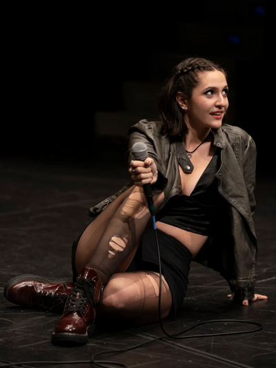 Monica Elena (actor, singer, model) sits on stage wearing a leather jacket after a performance.