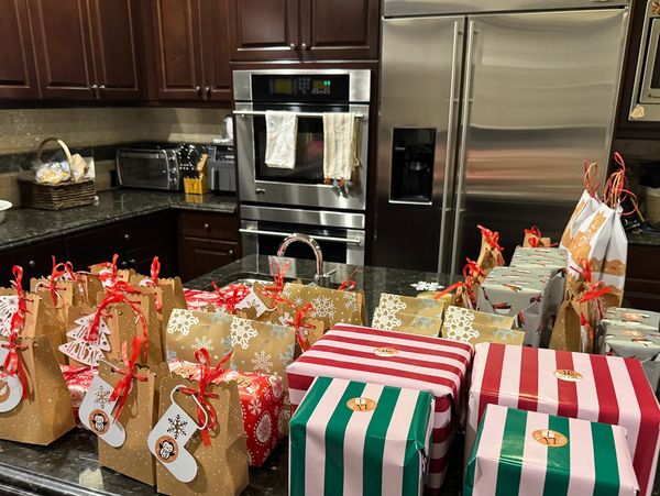 Christmas-themed gift bags and wrapped presents arranged on a kitchen counter.