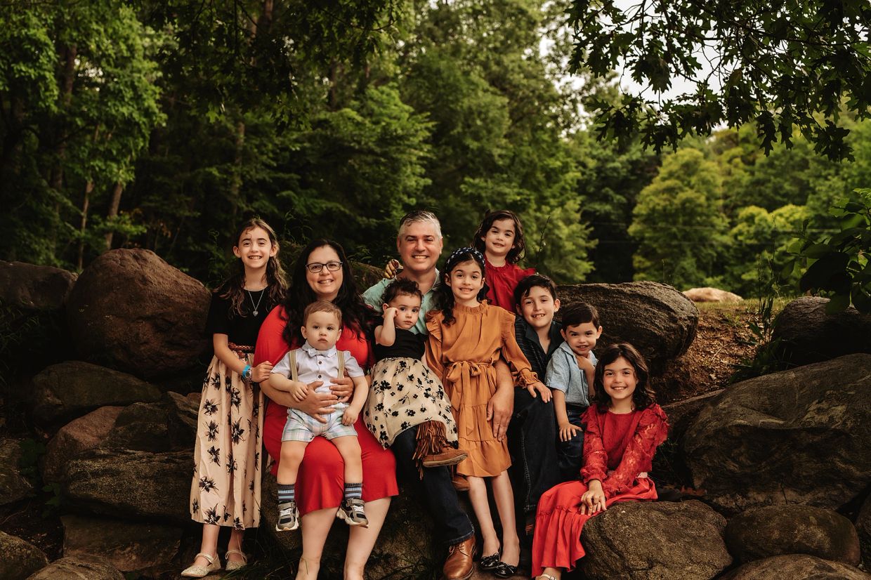 Family portrait outdoors on rock boulders with greenery.