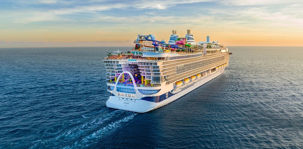 A large cruise ship named Icon of the Seas sails into the sunset on calm ocean waters.