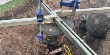 A hole in the ground with Sprinklers being levelled with a ground zero tool.