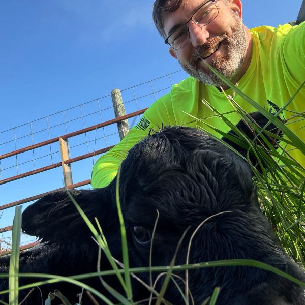 Man smiling with a black calf in the grass.