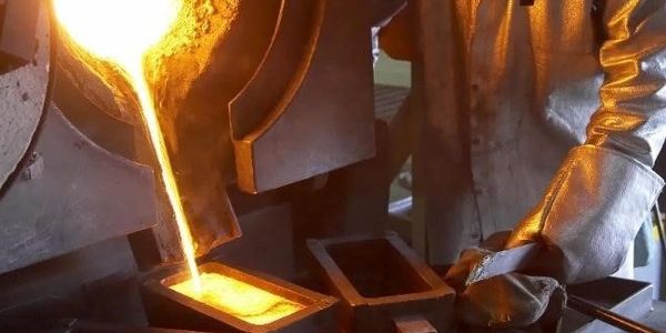 Molten metal being poured into a mold by a worker in protective gloves.