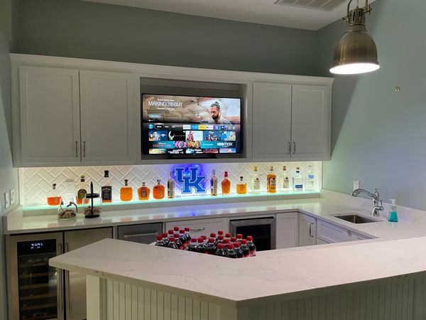Custom bar with backlit glass shelving custom cabinetry and quartz countertops with tile backsplash