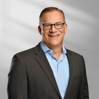 Smiling middle-aged man in glasses wearing a dark suit and light blue shirt.