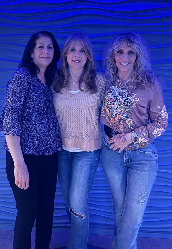 Three women posing together against a textured blue wall.