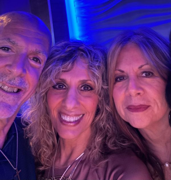 Three adults smiling in a close-up selfie with blue lighting.