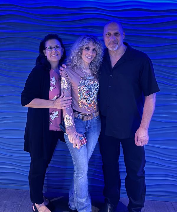 Three people posing happily against a blue textured wall.