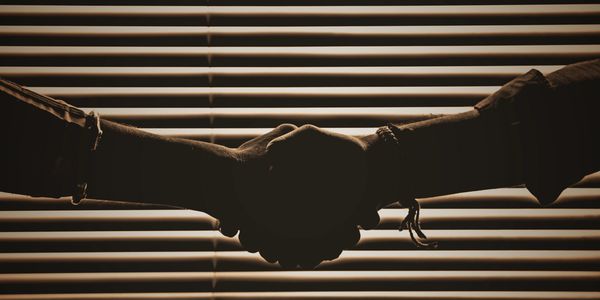 Two people shaking hands in front of window blinds.