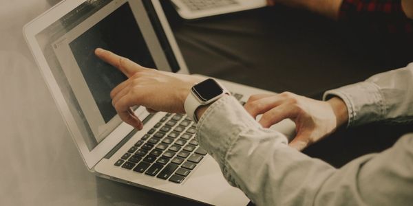 Person pointing at laptop screen during a discussion with another individual.