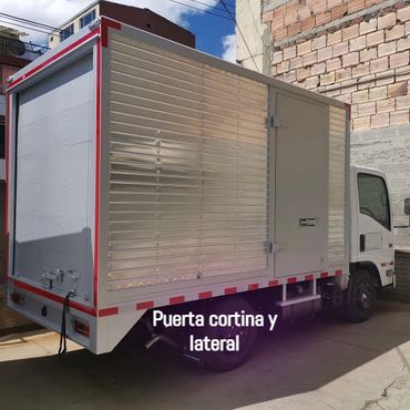 
Furgón con forros en aluminio acanalado, con puerta cortina posterior, y puerta lateral.
