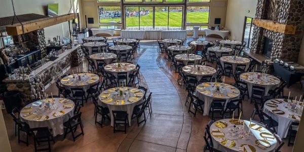 Rustic event hall with round tables and outdoor view.