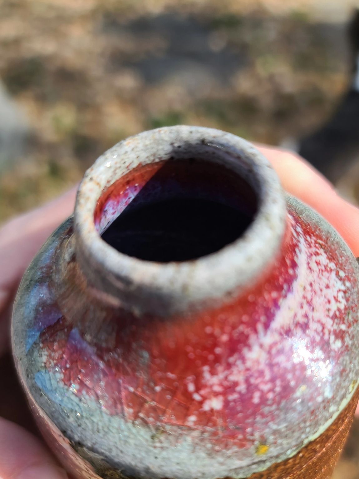 A ceramic bottle held by a white hand with a blurry background.