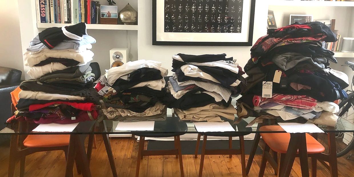 Four large piles of folded clothes on a glass table in a cozy living room.