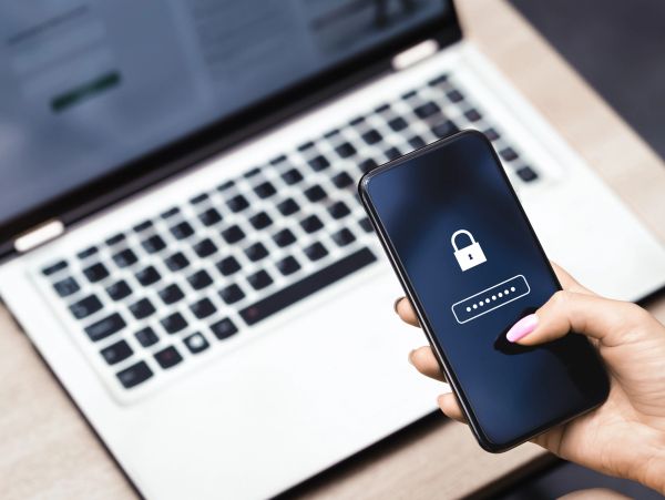 Person entering password on smartphone in front of laptop.