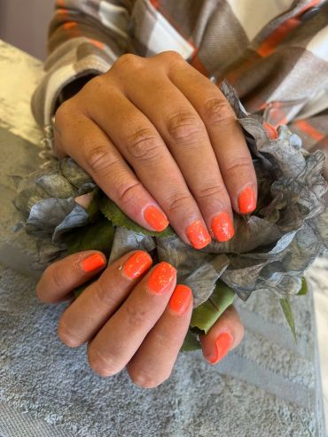 Hands with bright orange nail polish holding a gray decorative flower.