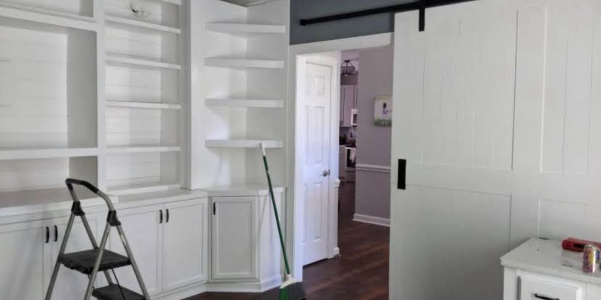 A clean, white room with built-in shelves, a step ladder, and a broom on dark wood flooring.