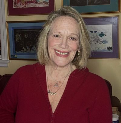 Smiling woman in a red top with framed artwork behind her.