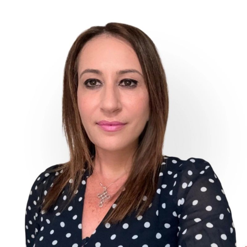 Woman with straight brown hair wearing a black polka dot blouse and a necklace.