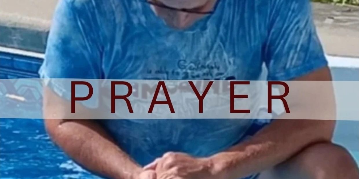 Man in blue shirt praying by the pool.