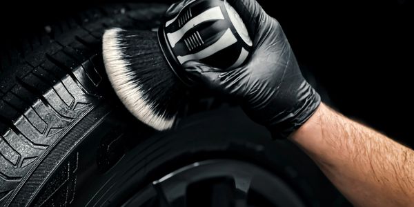Person cleaning a car tire with a brush wearing a black glove.