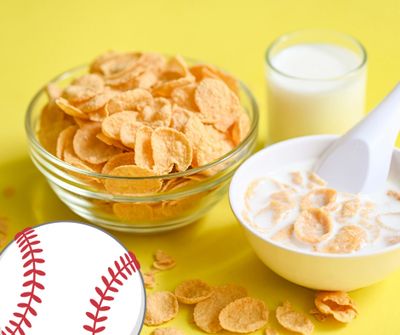 Cornflakes cereal with milk and a glass of milk on a yellow surface.