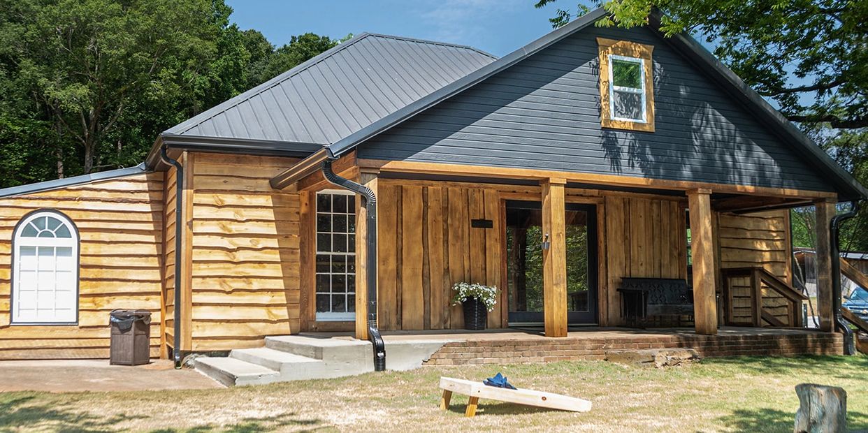 A rustic wooden house with a porch and a metal roof on a sunny day.