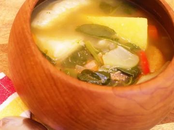 Wooden bowl filled with vegetable soup including greens and potatoes.