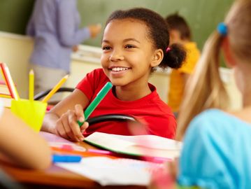 Smiling girl holding a green marker in a colorful classroom.
