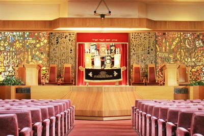 Interior of a synagogue with Torah scrolls on the bimah and stained glass windows.