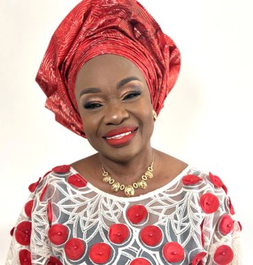 Smiling woman in vibrant traditional red and white attire with matching headwrap.