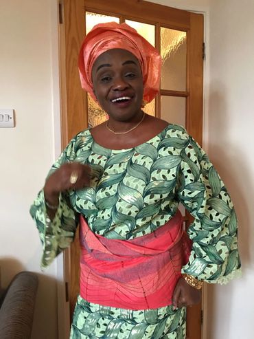 Woman dressed in vibrant traditional African attire smiling warmly.