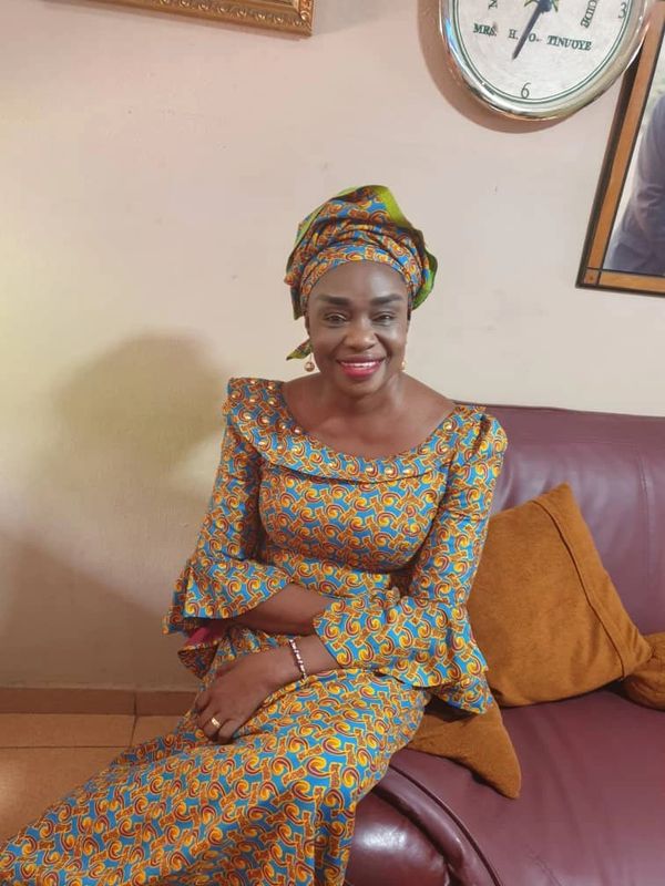 A smiling woman in vibrant traditional attire sitting on a couch.