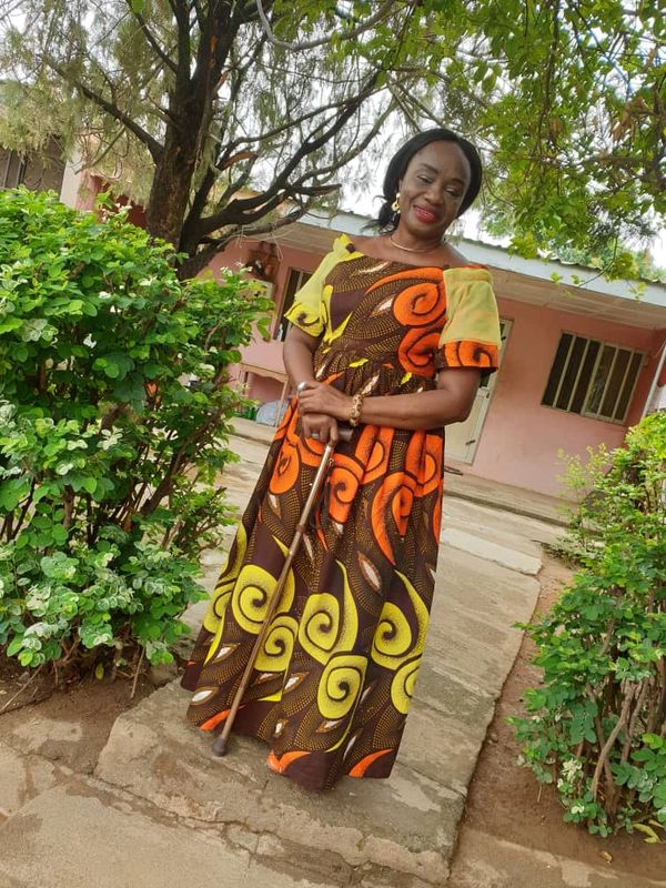 Woman in colorful dress standing outdoors with a walking cane, smiling.