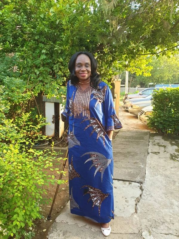A woman in a blue patterned dress standing outdoors with a walking cane.
