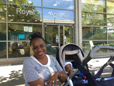 A smiling woman with a baby stroller outside the Royal Arsenal Medical Center.