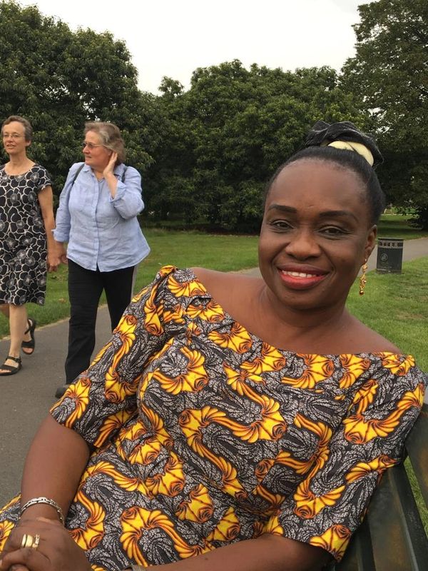 Smiling woman in vibrant yellow and black patterned dress sitting on a park bench.