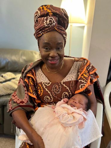 Woman in traditional attire holding a sleeping baby wrapped in a white blanket.
