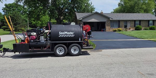 SealMaster trailer with equipment parked near a freshly sealed driveway in front of a house.