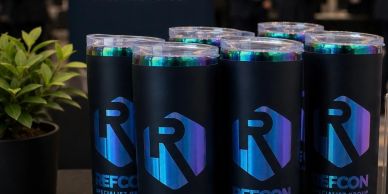 Black tumblers with a blue and purple 'R' logo and clear lids are displayed.