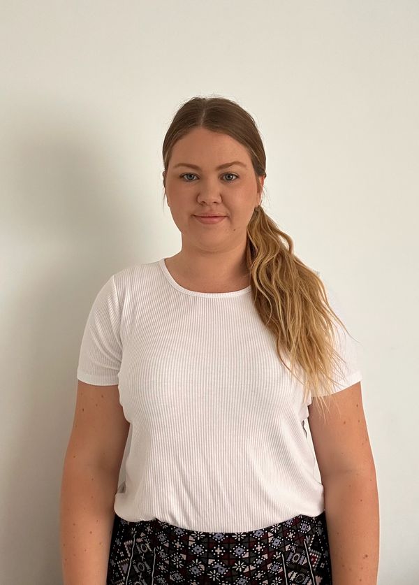 Woman with long blonde hair in a white shirt and patterned skirt.