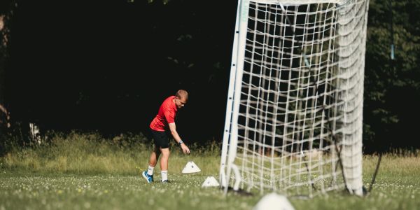 Man walking near soccer goal and cones on grass field.