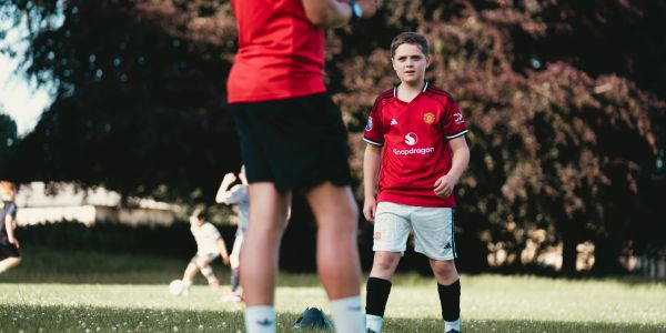 Boy in red soccer jersey playing soccer on grass field.