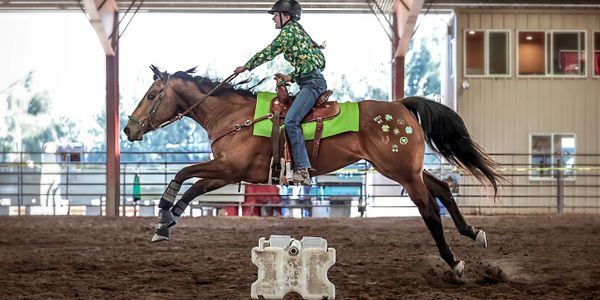 A rider and horse jumping over an obstacle in an indoor arena.