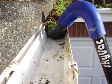 A blue nozzle attached to a vacuum is cleaning a gutter filled with debris.