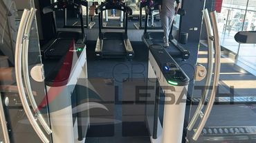 A person walking on a treadmill in a gym with entrance turnstiles.