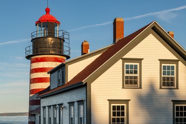 Red and white striped lighthouse beside a white building at sunset.