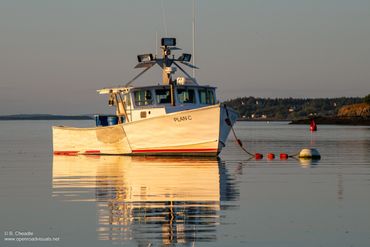 A small fishing boat named PLAN C floats calmly on still water at sunset.