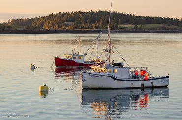 Two fishing boats docked on calm water during sunset.