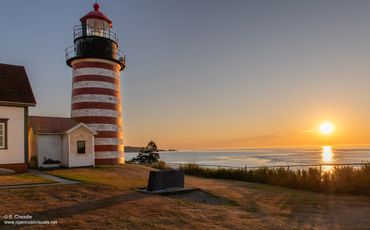 Striped lighthouse by the sea at sunset.